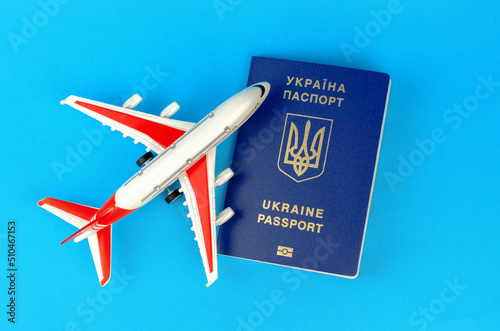 Ukrainian biometric passport and toy plastic plane on a blue background. Departure of Ukrainians abroad