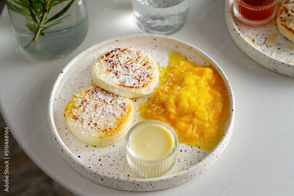 White plate with fried curd pancakes or syrniki, horizontal shot, sprinkled with coconut. White plate with fried curd pancakes or syrniki, horizontal shot, sprinkled with coconut.