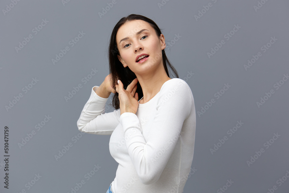an attractive woman stands on a gray background in a white T-shirt, carefully untangles soy hair an attractive woman stands on a gray background in a white T-shirt, carefully untangles soy hair