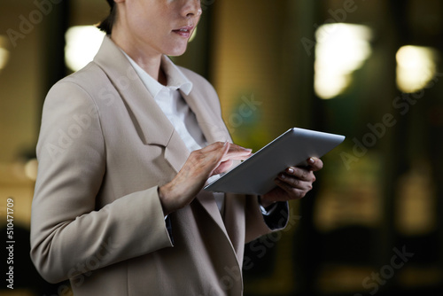 Close-up of contemporary businesswoman in jacket standing on night street and analyzing online file on tablet