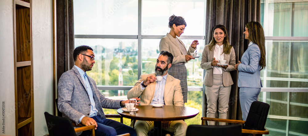 Coffee break at the office, two male colleagues talking and three young females drinking coffee