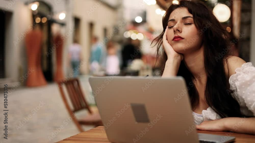 Close up view of tired exhausted boring young woman typing on laptop and falls asleep while sitting with a laptop at cafe. Close up view of tired exhausted boring young woman typing on laptop and falls asleep while sitting with a laptop at cafe.