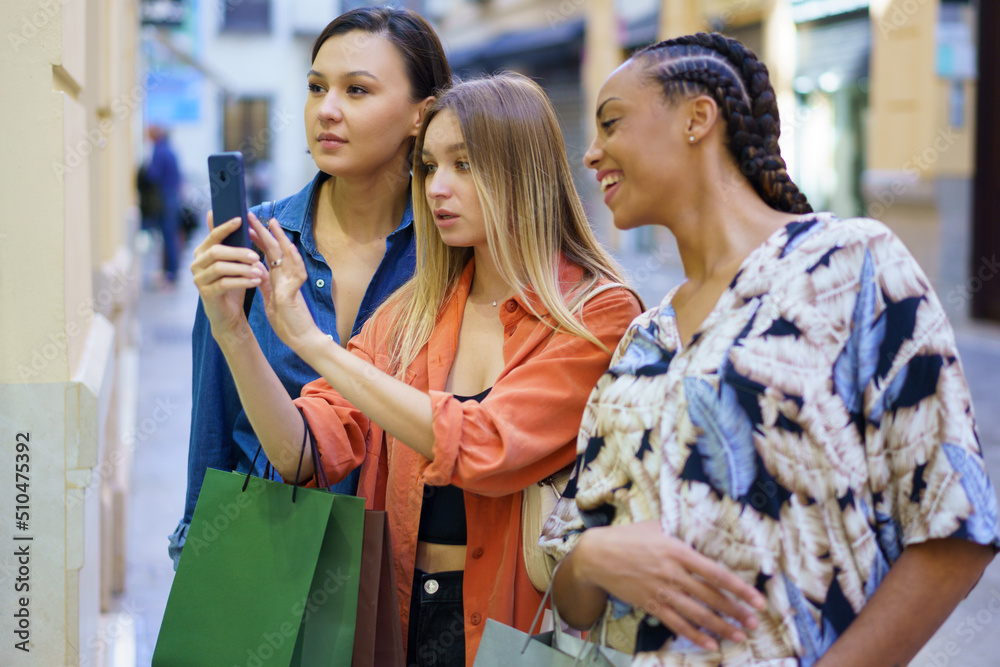 Multiracial women taking photo of showcase on smartphone Multiracial women taking photo of showcase on smartphone
