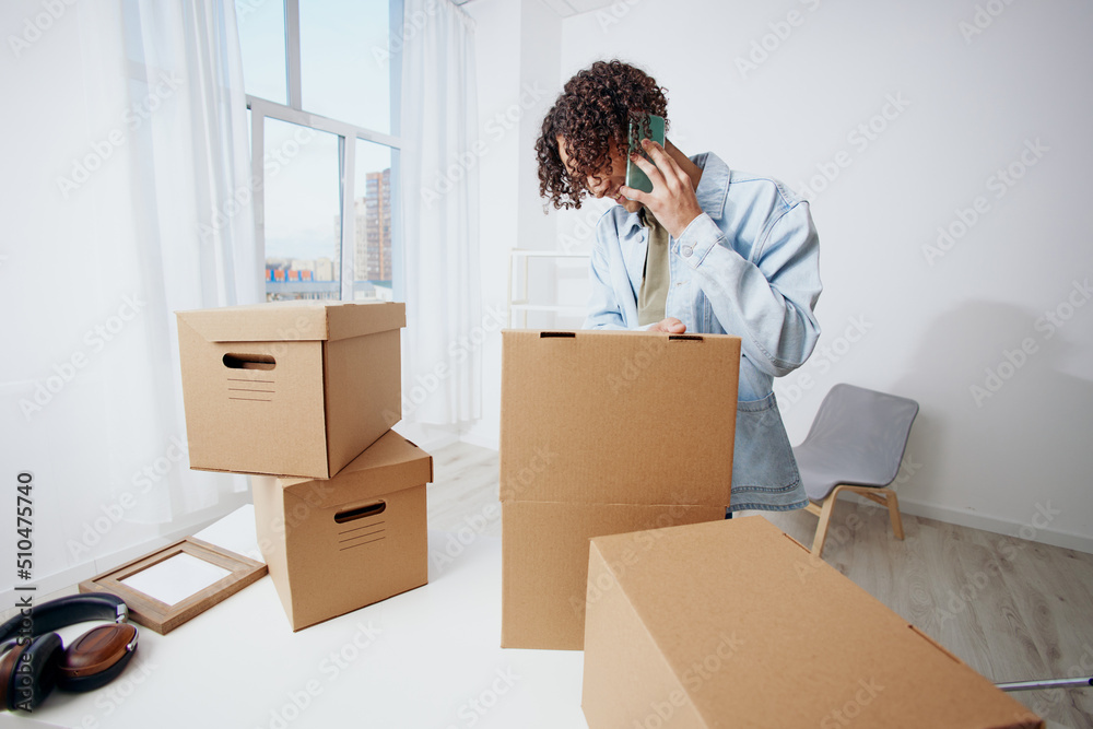 handsome guy cardboard boxes in the room unpacking with phone Lifestyle handsome guy cardboard boxes in the room unpacking with phone Lifestyle