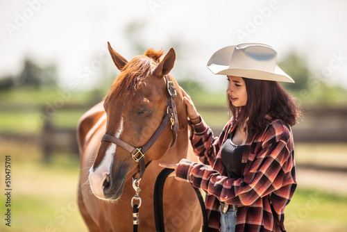Beautiful girl in a hat and checkered shirt talks to calm a paint horse out in a ranch