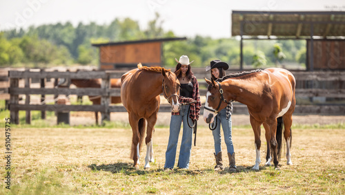 Two cowgirls meet their paint horses on a ranch on a sunny day