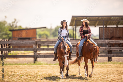Two cowgirls riding their horses on a ranch during hot summer day
