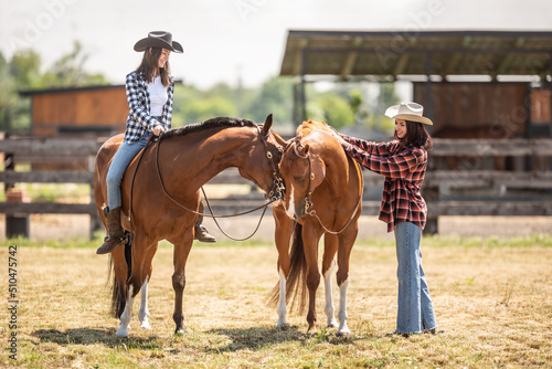 Fototapeta Naklejka Na Ścianę i Meble -  Two female friends on a ranch are getting ready for a horse ride