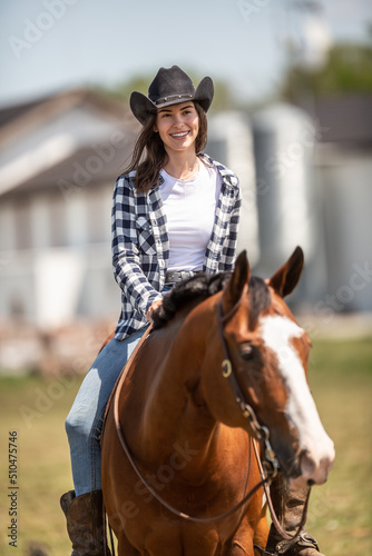 Beautiful smiling girl riding a paint horse, wearing a black cowboy hat © weyo