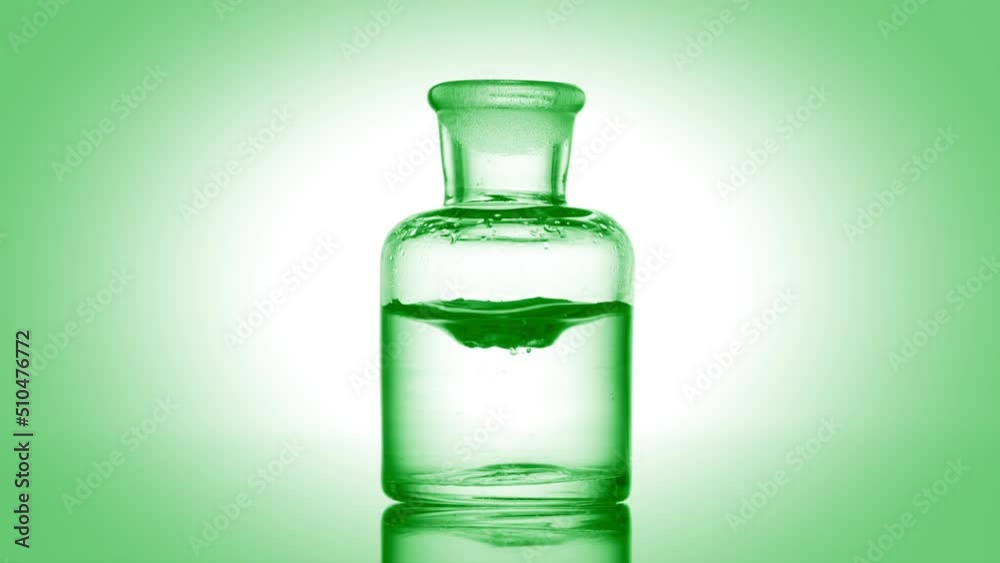 Green drop is falling into old fashioned bottle with green clear fluid on green background | Abstract skincare cosmetics with aloe vera extract mixing concept Green drop is falling into old fashioned bottle with green clear fluid on green background | Abstract skincare cosmetics with aloe vera extract mixing concept
