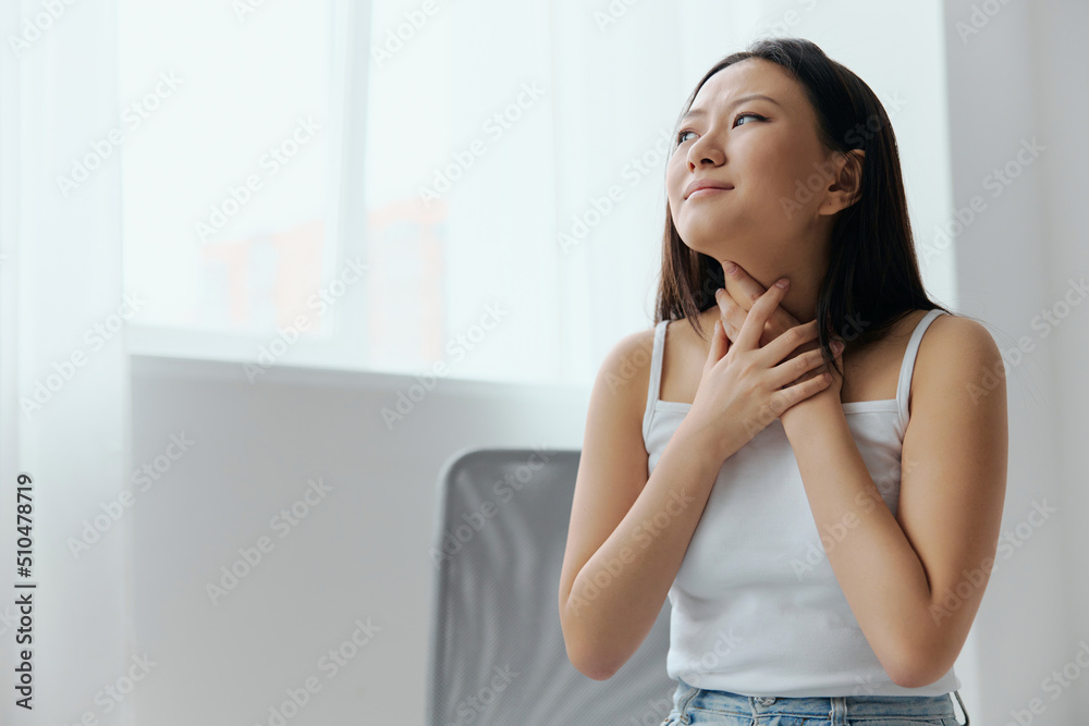 Sore throat Enlarged lymph nodes. Sad suffering tanned beautiful young Asian woman touch neck throat at home interior living room. Injuries Poor health Illness concept. Cool offer Banner Sore throat Enlarged lymph nodes. Sad suffering tanned beautiful young Asian woman touch neck throat at home interior living room. Injuries Poor health Illness concept. Cool offer Banner
