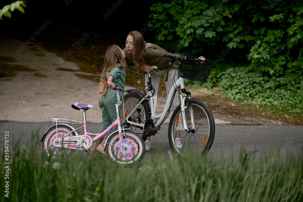 Naklejka premium Mom and daughter cycling in the park. Children summer vacation concept