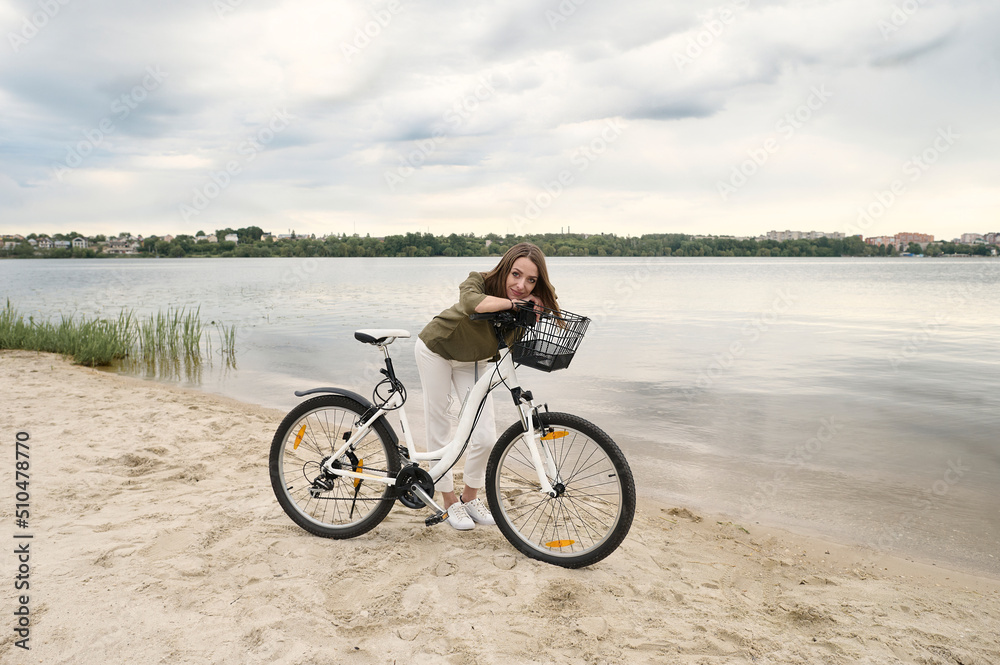 A portrait of a young beautiful girl with a bicycle on the river band