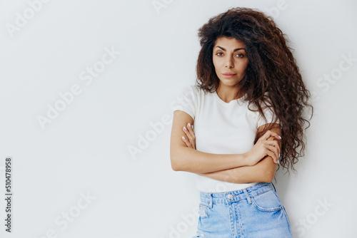 Gorgeous confident curly Latin female look at camera, crossing hands on the chest. Copy space for clothing fashion brands, free place for your ad. Studio shoot isolated over white background