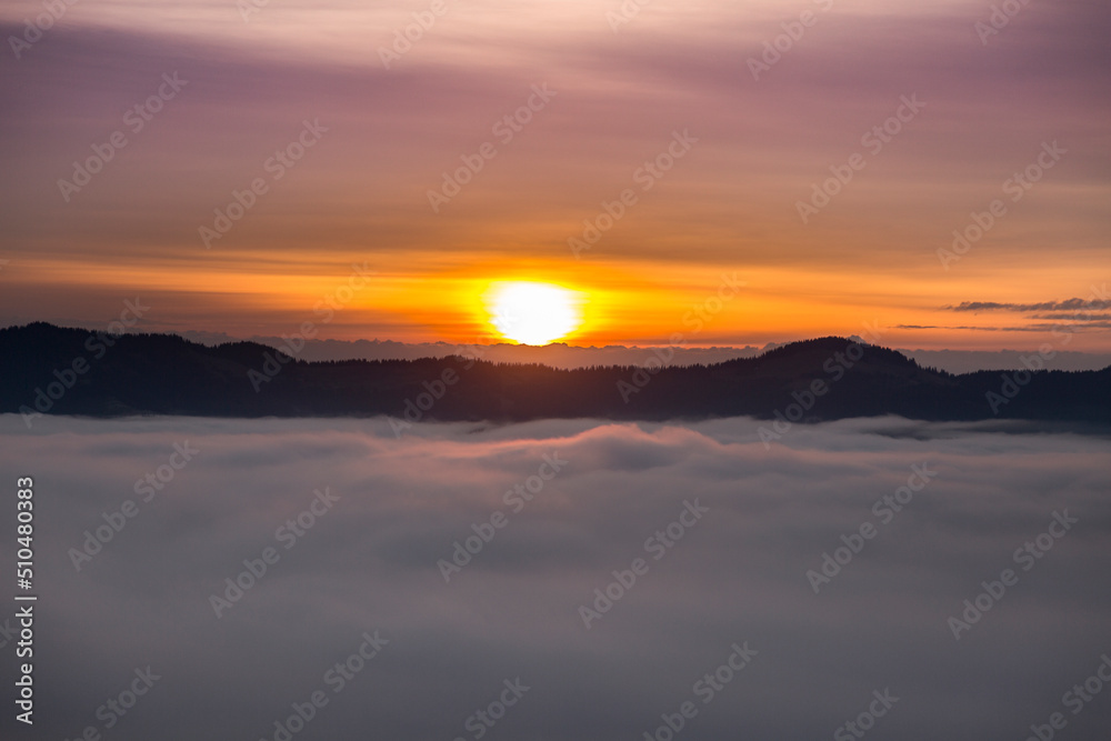 Morning orange sunbeams over misty clouds in the mountains