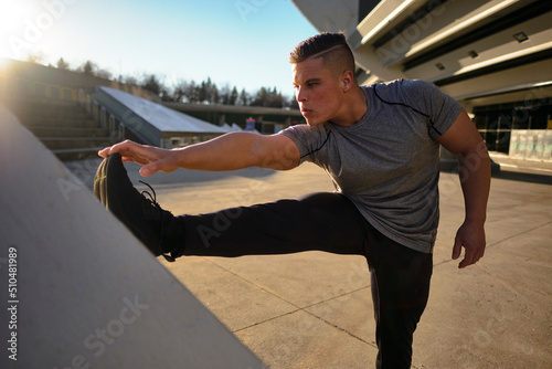 Male athlete stretching leg with sunset behind