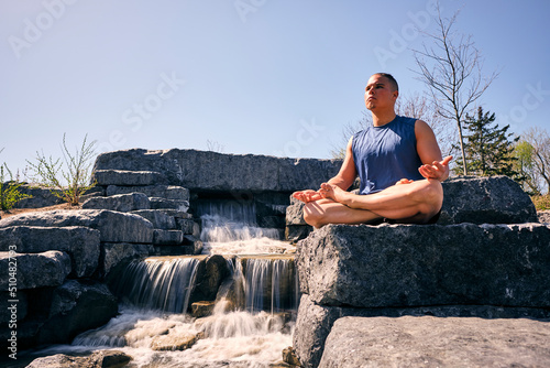 Young man meditating beside man made waterfall