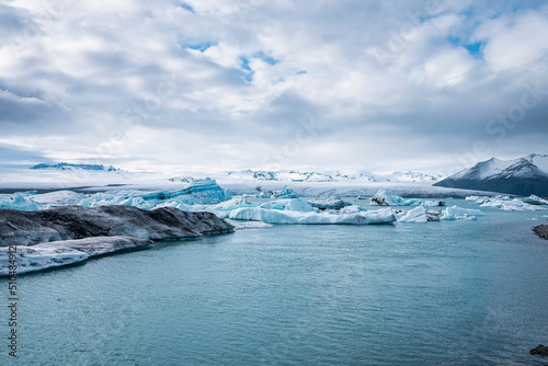 Scenic view of icebergs floating in Jokulsarlon glacier lagoon. Idyllic view of glacial ice formations against cloudy sky. View of global warming in Vatnajokull during extreme weather.