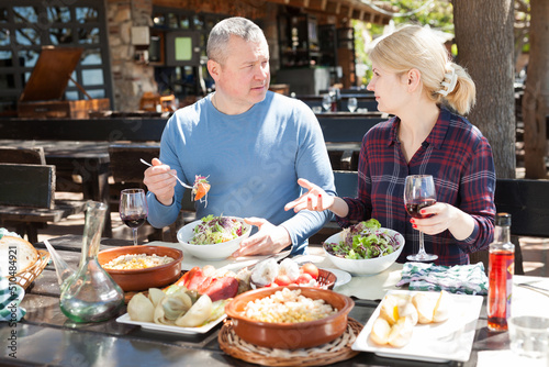 Family couple enjoying warm spring day and delicious dinner with wine in cosy country restaurant in open air