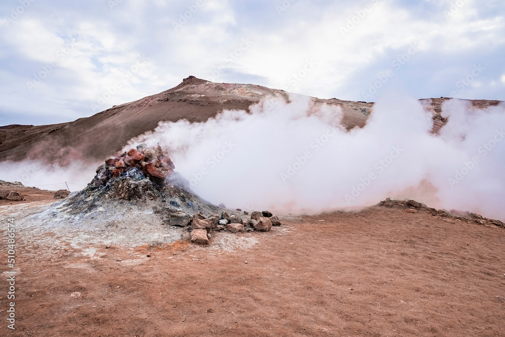Steam emitting from fumarole in geothermal area of Hverir. Sulphur dioxide erupting from volcanic crater at Namafjall. Geyser in famous tourist attraction against cloudy sky. Steam emitting from fumarole in geothermal area of Hverir. Sulphur dioxide erupting from volcanic crater at Namafjall. Geyser in famous tourist attraction against cloudy sky.