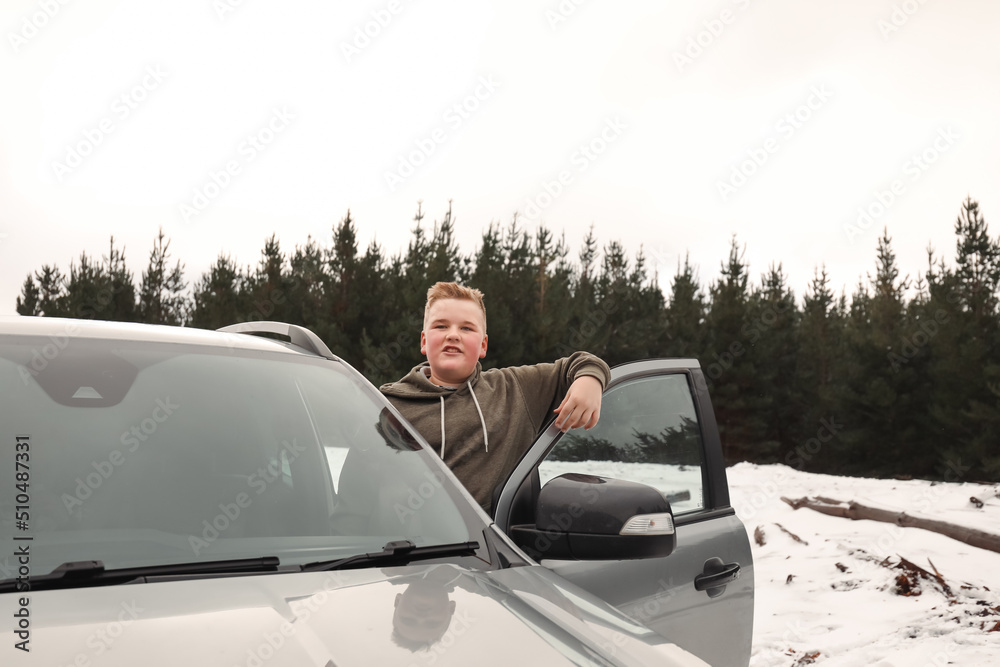 Happy preteen boy standing on side of vehicle smiling in the snow on cold winter drive