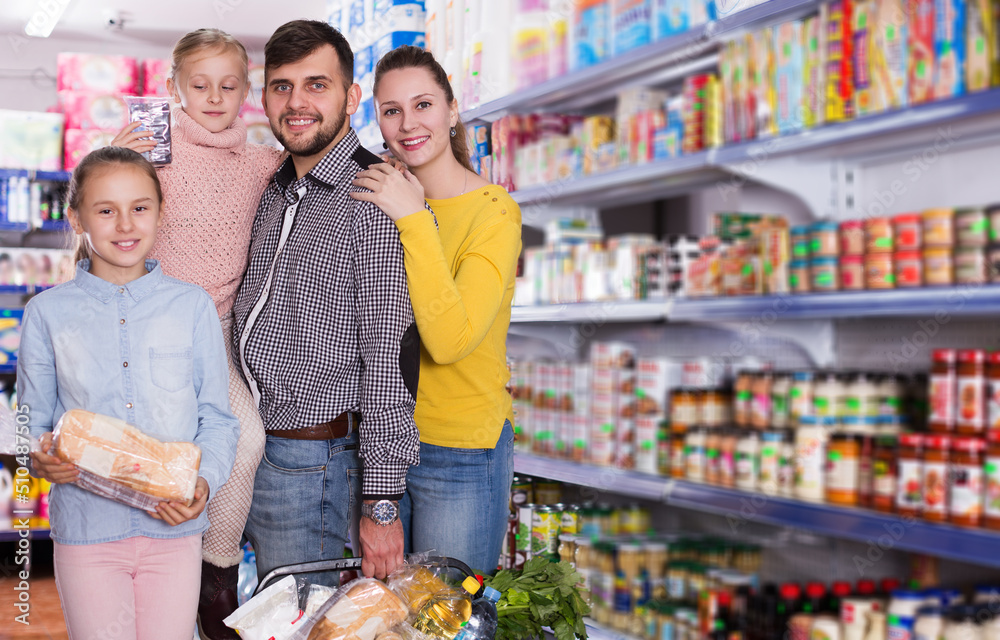young parents with two little girls with purchases during family shopping in grocery store
