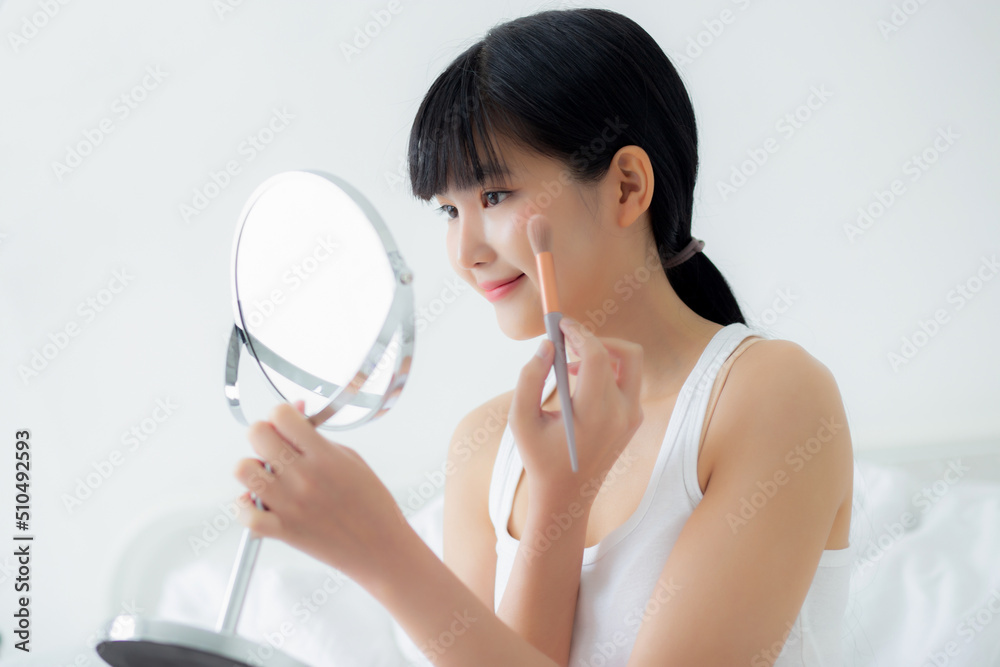 Beautiful young asian woman applying brush on cheek makeup of cosmetic looking mirror on bed, beauty of girl with skin facial and wrinkle in the bedroom, cosmetology for female, skincare concept. Beautiful young asian woman applying brush on cheek makeup of cosmetic looking mirror on bed, beauty of girl with skin facial and wrinkle in the bedroom, cosmetology for female, skincare concept.