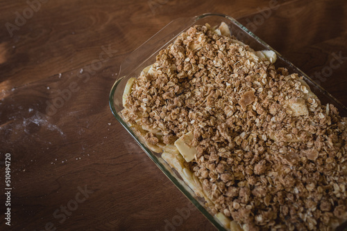 Prepared, unbaked apple crisp sitting on a brown table with flour and crumbs on the table