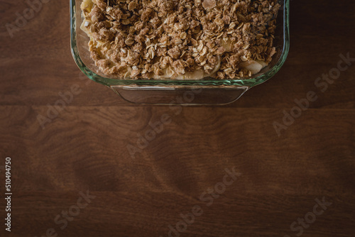 View of part of a pan of prepared, unbaked apple crisp sitting on a plain, brown table