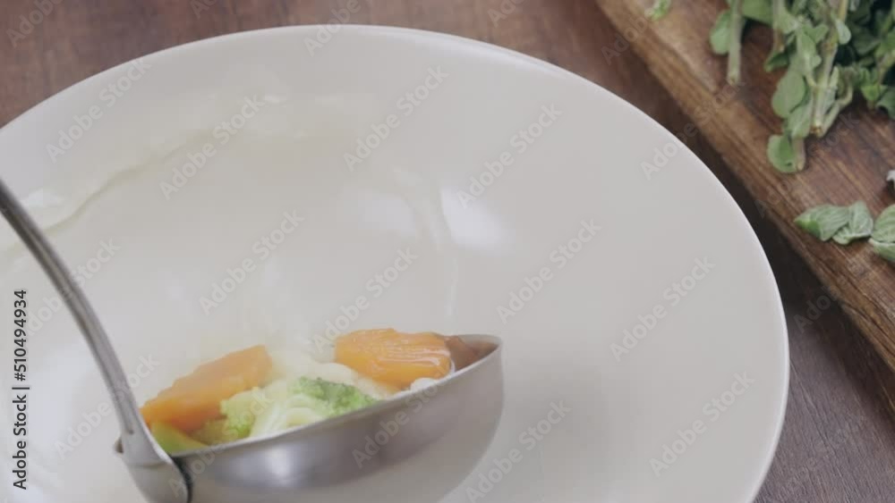 pouring soup into a bowl colorful vegetables carrot, broccoli vegetarian meal slow motion