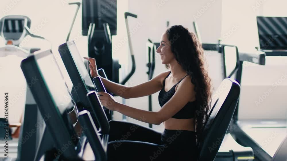 Sporty lifestyle. Young active lady turning on training mode on bicycle apparatus and start exercising, slow motion Sporty lifestyle. Young active lady turning on training mode on bicycle apparatus and start exercising, slow motion