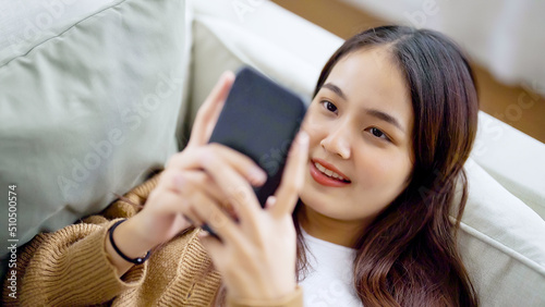 Happy young asian woman relax on comfortable couch at home texting messaging on smartphone  smiling girl use cellphone  browse wireless internet on gadget  shopping online from home