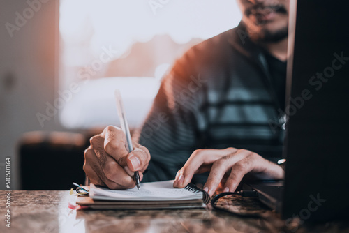 Young man writing in notebook from living room at home