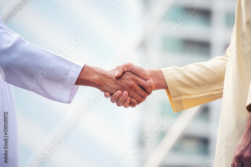Arab Businessman Muslim dress shaking hands together. Muslim Men Teamwork business partner handshake with business Partnership. Close up hand UAE diversity multiracial people trust honesty commitment