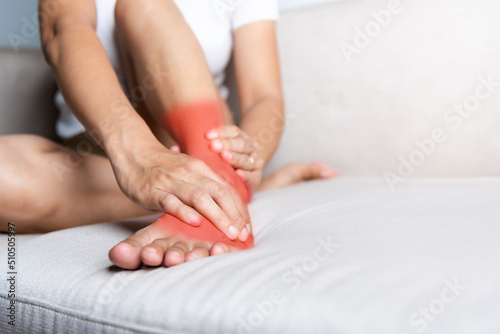 Foot pain, Asian woman sitting on sofa hold her ankle injury feeling pain in her foot at home, female suffering from feet ache use hand massage relax muscle from ankle interior, Healthcare and medical © sorapop