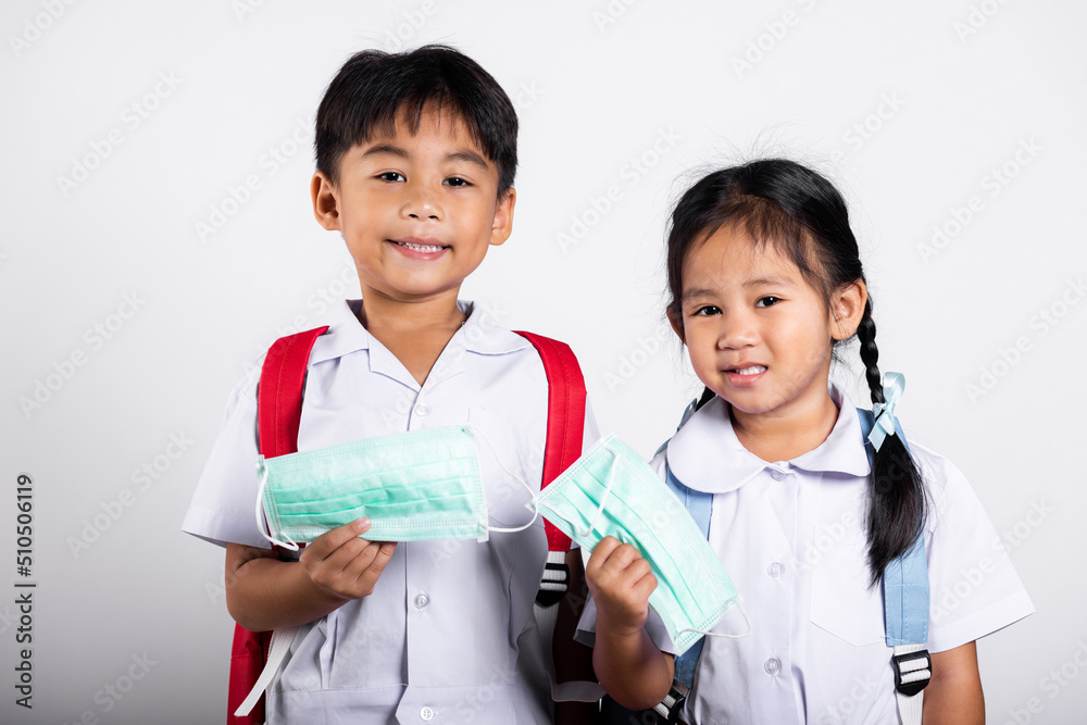 Two Asian student kid girl boy brother sister wearing student thai uniform holding protect mask ready to go to school in studio shot isolated on white background, new normal back to school Two Asian student kid girl boy brother sister wearing student thai uniform holding protect mask ready to go to school in studio shot isolated on white background, new normal back to school