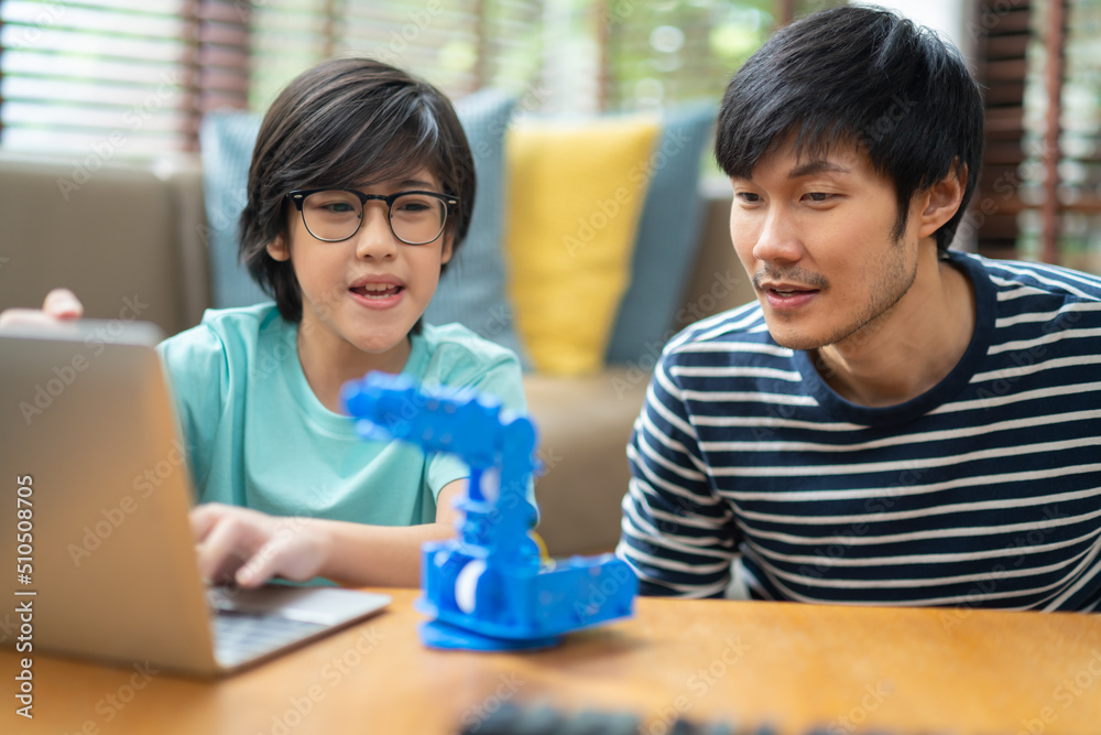 asian boy child with father successful control robot arm on Digital tablet and computer keyboard, happy family getting a lesson in coding control robotics at home.study at home concept. asian boy child with father successful control robot arm on Digital tablet and computer keyboard, happy family getting a lesson in coding control robotics at home.study at home concept.