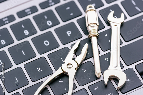 Computer hardware service and maintenance concept : Open-end wrench, a screwdriver, a needle-nose plier on a computer keyboard, depicts repairing, software updating or changing to a newer version. photo