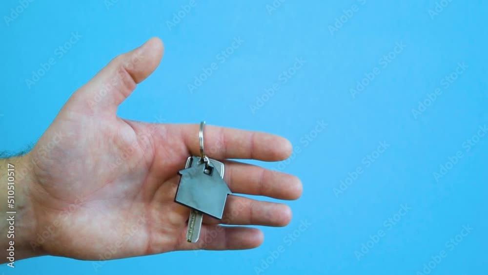 The man hand holds the keys with the house keychain on blue background. Purchase of apartments. The man hand holds the keys with the house keychain on blue background. Purchase of apartments.