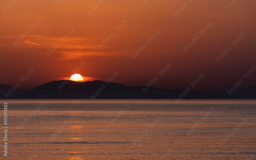 Sea beach and colorful sunset sky. Panoramic beach landscape. Tropical beach and seascape and a distant island in the background. Orange and golden sunset sky, calmness, tranquil relaxing summer mood.