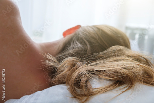 Portrait of young woman lying in bed, back view. Wild hair on pillow in morning sun rays. Tenderness and good morning concept, close up