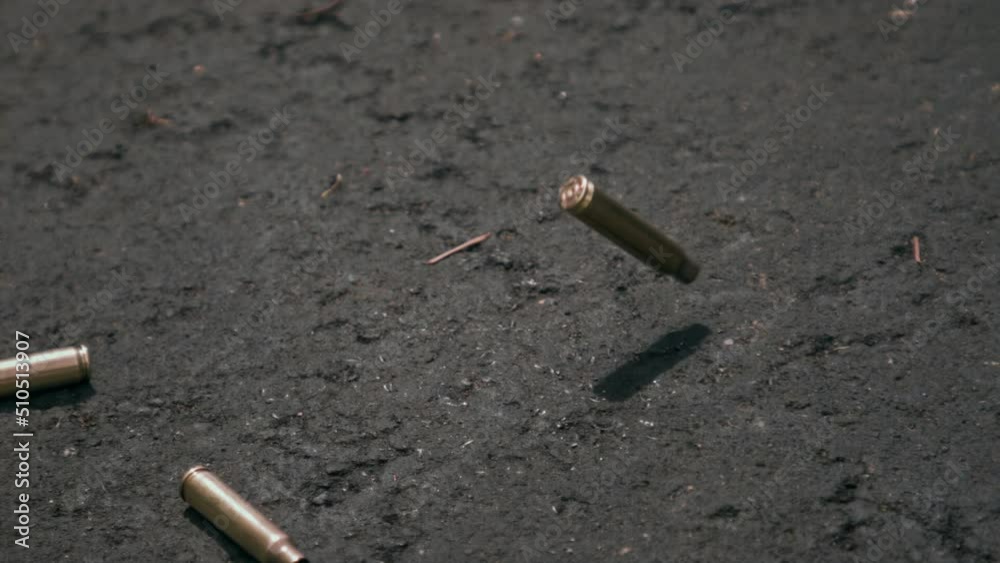 Empty bullet shell casings falling on asphalt ground in 1000fps slow motion