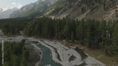 Aerial, flying in top of a river in the middle of a pine forest in the Himalayas, mountains with snow in the  back of the forest, drone goes down slowly. Kumrat, KPK, Pakistan photo