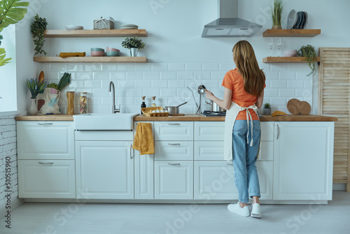 Full length rear view of young woman cooking at the domestic kitchen