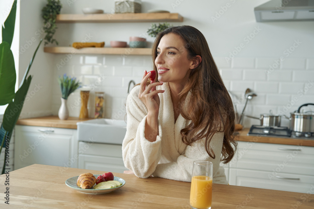 Happy young woman in bathrobe having breakfast at the modern kitchen Happy young woman in bathrobe having breakfast at the modern kitchen