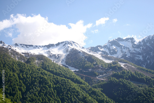 Mountains in snow and forest in spring. Blue sky and clouds background © sparklet