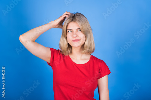 Young and attractive caucasian blonde girl in casual clothes with a hand on her head is thinking isolated on a blue studio background. Memory concept.