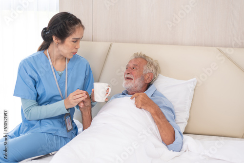 Caring nurse helping sick elderly man to drink in bed in a nursing home.