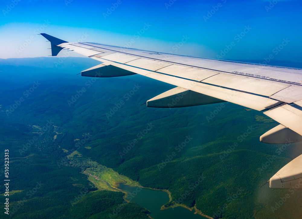 View of airplane wing, blue skies and green land during landing. Airplane window view. View of airplane wing, blue skies and green land during landing. Airplane window view.