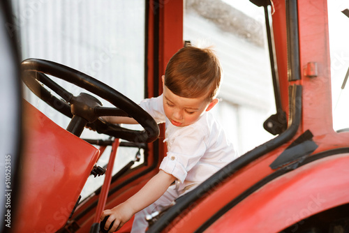Funny little boy of two years sitting in tractor in summer, outdoors